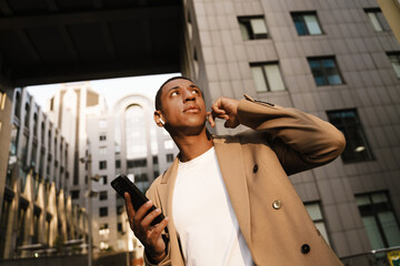 Black man in earphones using cellphone while walking at city street