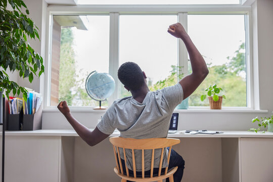 Rear View Of Man Working From Home On Computer  In Home Office Stretching At Desk