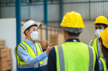 The factory employee consists of engineers, foreman, technicians, and related department staff. Wear a mask, hard hat, and vest. meeting before starting work inside the warehouse. Teamwork concept.