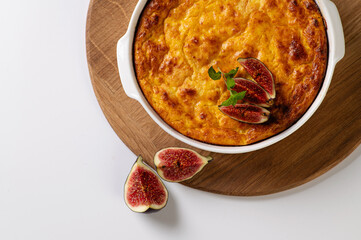 pumpkin cheese casserole in a round white shape on a wooden board to serve on a white table, top view, space for text