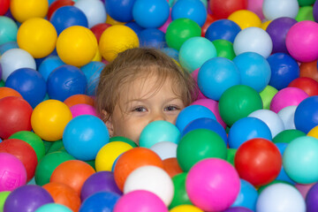 Head of happy caucasian little girl of five years old among multicolor balls in play center