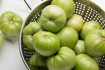 Green tomatoes for conservation in a colander on a white marble background. Unripe tomatoes for harvesting.