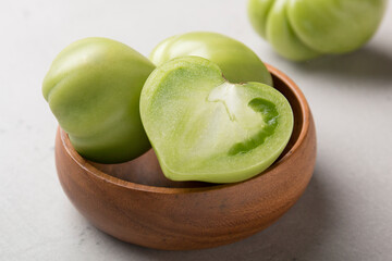 Green tomatoes for conservation in a wooden plate on a gray background. Unripe tomatoes for harvesting. Cutaway tomato.