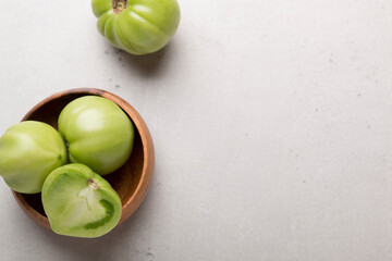 Green tomatoes for conservation in a wooden plate on a gray background. Unripe tomatoes for harvesting. Cutaway tomato.