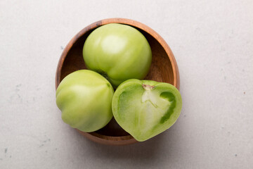 Green tomatoes for conservation in a wooden plate on a gray background. Unripe tomatoes for...