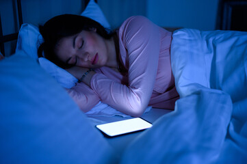 Woman lying in her bed during night and sleeping while her smartphone