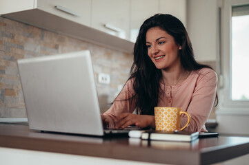 Woman in pajamas using a laptop and drinking coffee in the morning at home