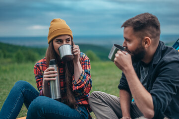 Couple of campers drinking coffee from a metal cups and a thermos in the nature