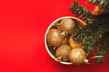 Gold balls and toys in a white cup with a branch of a Christmas tree on a red background