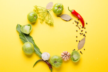 Green tomatoes for conservation with spices on a yellow background. Unripe tomatoes for harvesting. Pepper, garlic, allspice, cloves, horseradish, spices, bay leaf.