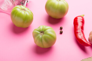 Green tomatoes for canning with spices on a pink background. Unripe tomatoes for harvest. Pepper, garlic, allspice, cloves, horseradish, spices, bay leaf.