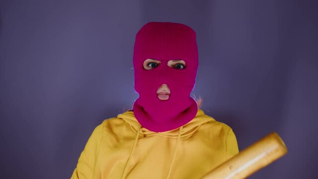 Young woman in pink balaclava with baseball bat. Hooligan in mask with bat in hands.