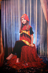 Small girl during a stylized theatrical circus photo shoot in a beautiful red location. Young model...