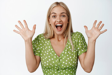 Happy and surprised blond girl cheering, celebrating, hear great announcement and rejoicing, standing over white background