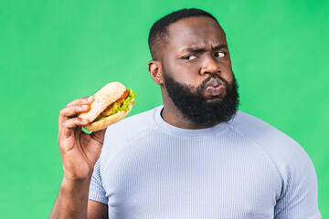 Hungry young african american black man eating hamburger isolated over green background. Diet concept.