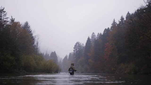 Man standing in the river swinging fishing rod, fly fishing on a autumn rainy day