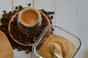 a glass glass stands on coffee beans in a wooden plate next to a sugar bowl with brown sugar