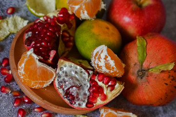 A pomegranate, whole and broken into pieces with other fruits, lies on a marble table