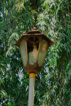 an ancient lamp with its glass is broken. a lamp in the park that possibly illuminates at night. old lamp that is not properly maintained.