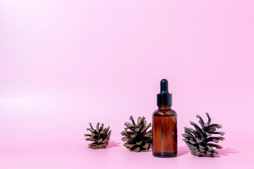Obraz na płótnie Canvas Brown glass serum bottle with pipette and pine cone on pink background with copy space. Body care serum cosmetic skin care. Front view with copy space.