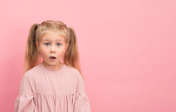 Little surprised funny girl with mouth open on pink background with copy-space.