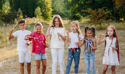 A large group of cheerful children play in the Park and inflate soap bubbles. Games in a children's camp - Powered by Adobe