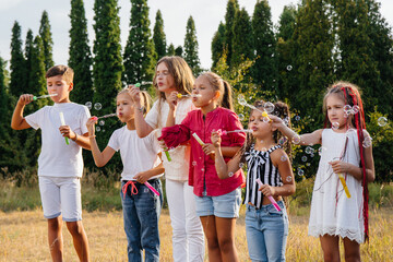 A large group of cheerful children play in the Park and inflate soap bubbles. Games in a children's camp