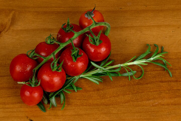 baby fresh red tomatoes, arranged sideways with green branches, fine herbs on the side on the wooden table, photo from above, space for text