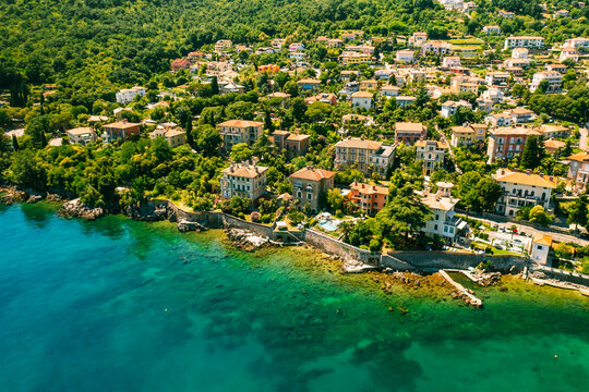 Beautiful villas near the coast of rocky beach in a small town Lovran, Croatia. Arial view of Lungomare sea walkway with transparent water.