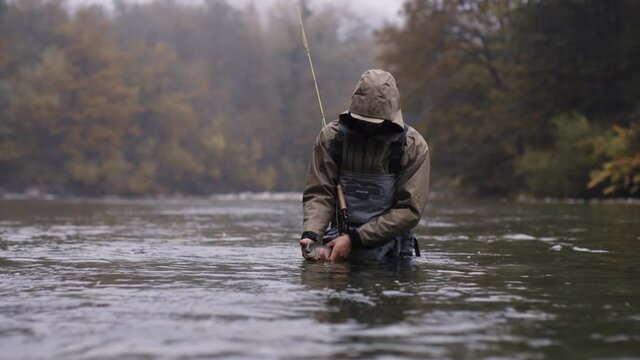 Man standing in the holding fishing rod, fly fishing on a autumn rainy day, holding a fish