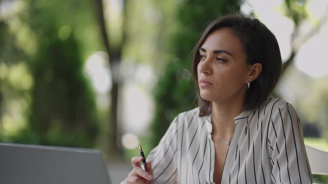Pensive woman Brunette arabic Hispanic ethnic group sits at a table in a summer cafe with a laptop. Serious business woman pondering problem solving and business development strategy