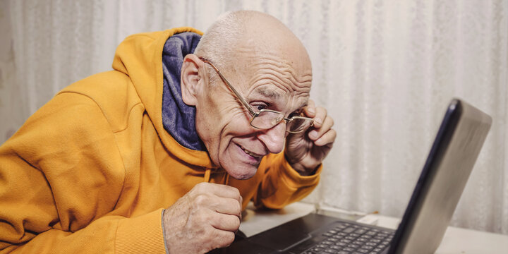 Mature man taking off glasses to look at laptop reading online news at home