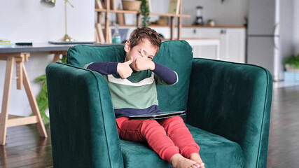 Cheerful little boy smiling while sitting on couch and using tablet at home. Modern kid and education technology. little boy looking at touch pad at home.