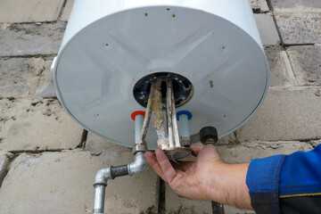 Repair and maintenance of boilers. The plumber pulls the tubular electric heater out of the hole in...