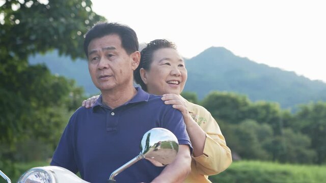 Asian senior couple enjoy their weekend by riding scooter along beautiful nature scenic, life after marriage relationship goal, middle age lover showing relax and happy doing outdoor activity together