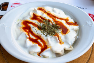Manti, Turkish traditional ravioli dumpling like food with yoghurt and tomato sauce in plate, close-up selective focus
