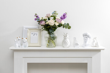 Bouquet of hackelia velutina, purple and white roses, small tea roses, matthiola incana and blue iris in glass vase is on the white coffee table . Grey wall