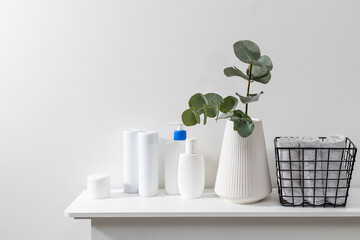 Bathroom interior. Metal basket with rolled face towels, white grooved vase with eucalyptus branch, shampoo and cream jars on shelf in the spa salon