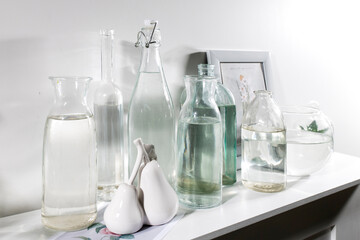 A set of bottles of different shapes with water with a photo frame is on the chest of drawers
