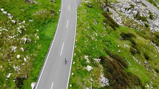 Bird's eye aerial of active wheelman ride on transport bike on serpentine hairpins roadway, drone above view of male cycler on bicycle exploring world during getaway travel for recreation
