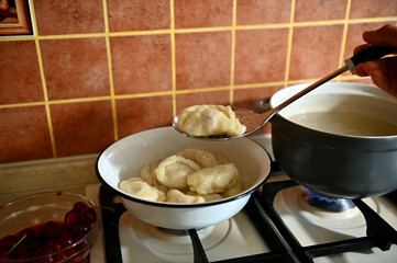 The pastry chef takes out cooked dumplings from boiling water into a colander
