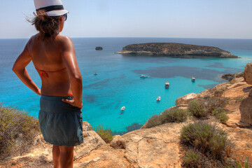 Girl in front of the Island of Rabbits in Lampedusa, Sicily, Italy - obrazy, fototapety, plakaty
