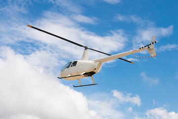 White helicopter flying against the backdrop of clouds in clear sunny weather