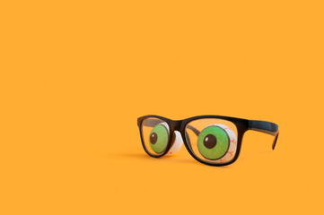 Funny Halloween concept with eyeglasses and doll eyes on orange background