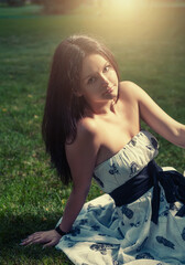 Dark haired women sitting on green grass half in shadow