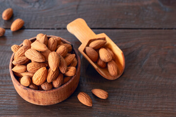 almonds in a wooden bowl and a scoop close-up. background with almonds. almonds on a wooden background.