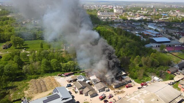 Aerial view of firefighters extinguishing ruined building on fire with collapsed roof and rising dark smoke.