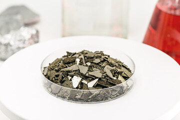Manganese samples in petri dish, pure manganese metal flakes used in industry, isolated white background.