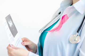 Woman doctor with pink ribbon on white medical uniform holds results of ultrasound scan in her...