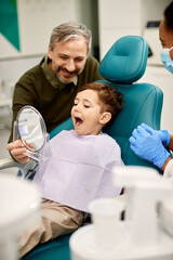 Little boy looking his teeth in a mirror after dental procedure at dentist's office.